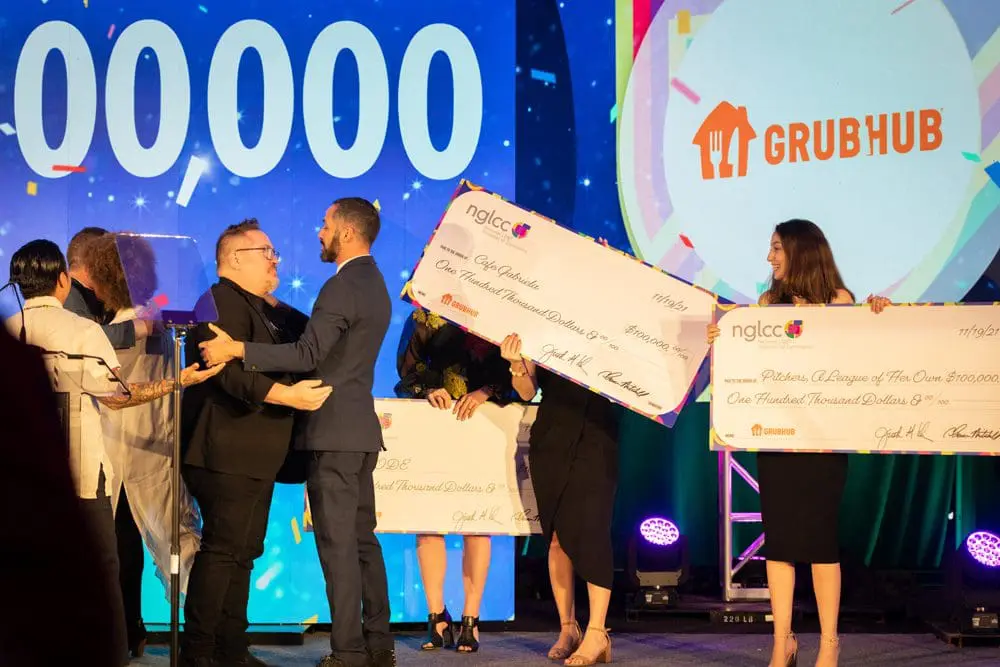 Three NGLCC employees giving away checks to a group of corporate partners on stage.