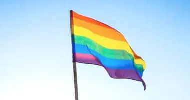 Pride flag waves in front of a blue sky.