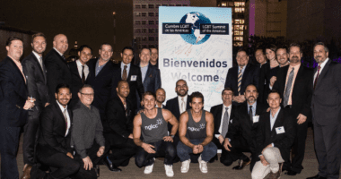 A group of men pose in front a sign that reads, "Bienvenidos - Welcome!"