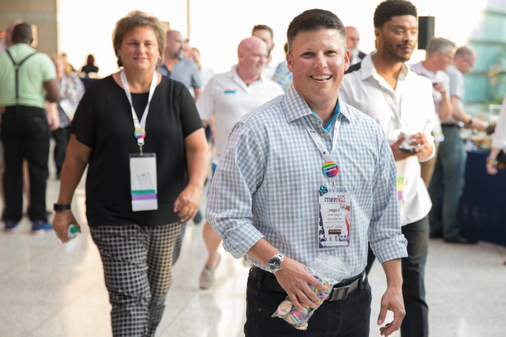 A white male smiling at the camera, holding a bag of pins, while attending and NGLCC event.