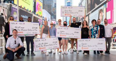 A group of LGBT business owners hold large checks from NGLCC, nglccNY, and Grubhub in the center of Times Square.
