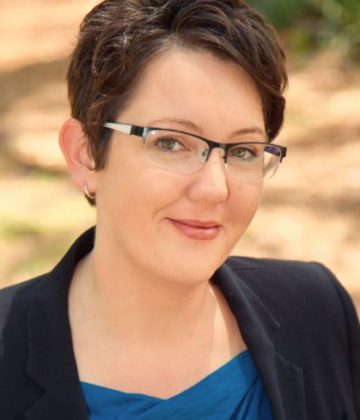 Kellie Parkin headshot. A woman with short brown hair, glasses, black blazer, and a blue shirt smiles at the camera.